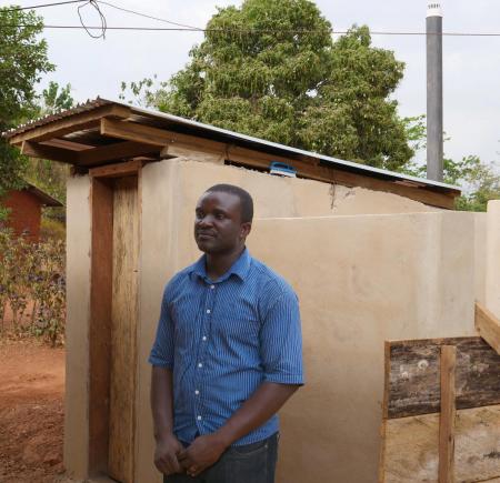 Festus Baudi, World Vision, outside the chief's household toilet  in Panaaba