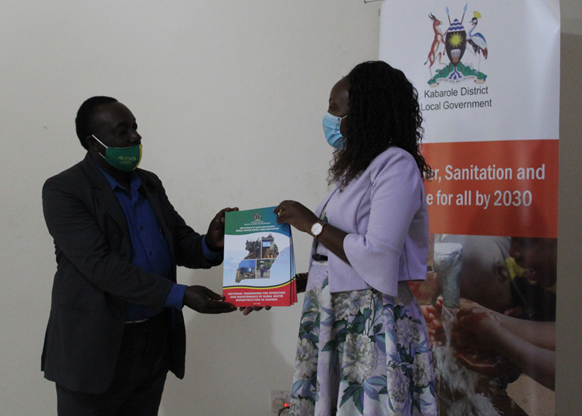 MWE official handing over copies of the O&M framework to Ms Pamela Kabasinguzi - Program Manager for Caritas Fort Portal HEWASA during its launch in 2020